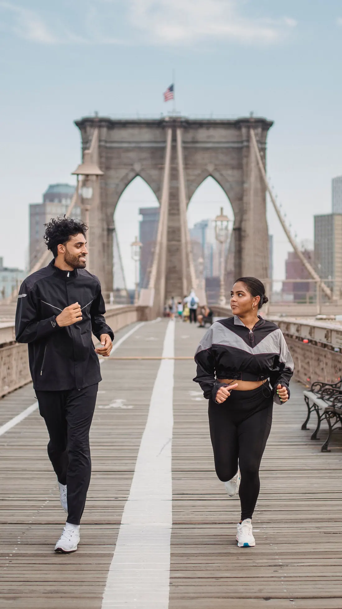 A man and a woman smiling as they run together across the Brooklyn Bridge