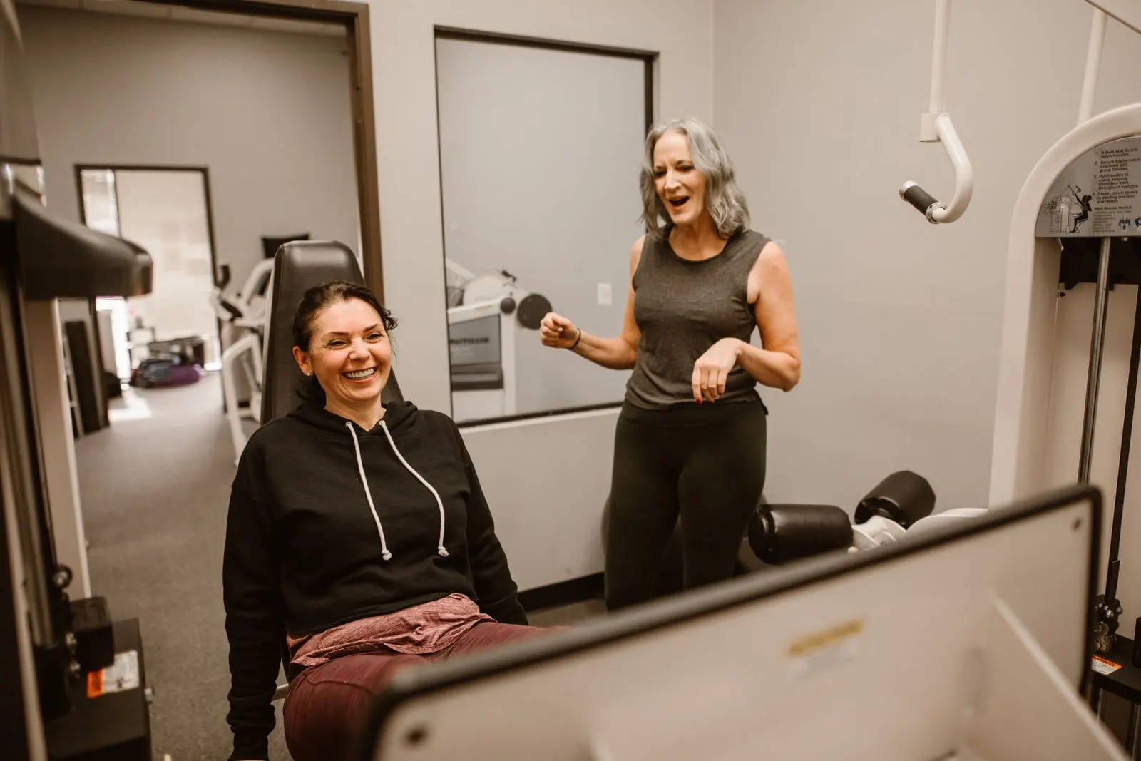 A trainer and her client laughing together between sets at the gym